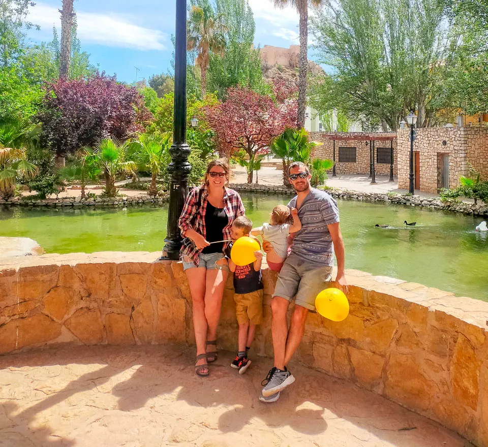 La familia con globos amarillos en una glorieta junto a un estanque con palmeras