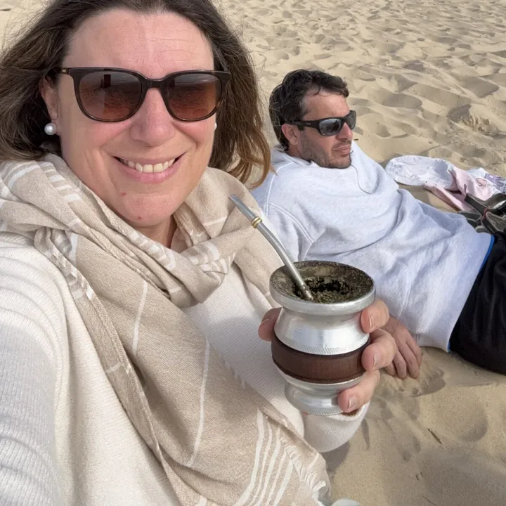 Selfi de Flor con el mate en la mano y Juan recostado en la arena
